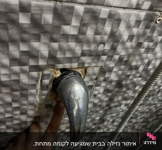 ברז מתכת בקיר אריחים עם אצבע מצביע על חיבור